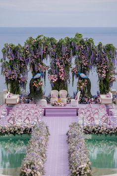 an outdoor wedding setup with purple flowers and greenery on the wall, overlooking the ocean