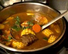 a pot full of soup with corn and carrots on the side, next to a spoon