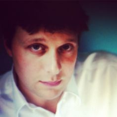 a close up of a person wearing a white shirt and looking at the camera with a serious look on his face