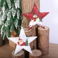 two wooden stars decorated with santa claus and snowmen are sitting on logs next to a christmas tree