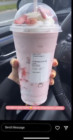 someone holding up a pink drink in their hand with strawberries and cream on it