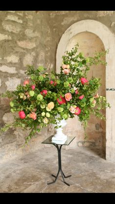 a vase filled with lots of flowers on top of a table next to a stone wall