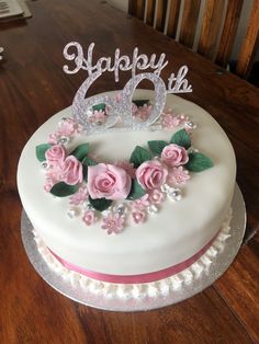 a white cake with pink flowers and a happy birthday sign on top is sitting on a wooden table