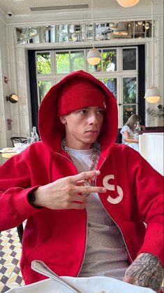 a man in a red hoodie sitting at a table with a plate of food