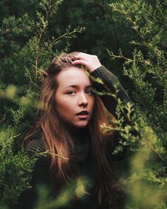 a woman is standing in the woods with her hands on her head and looking at the camera