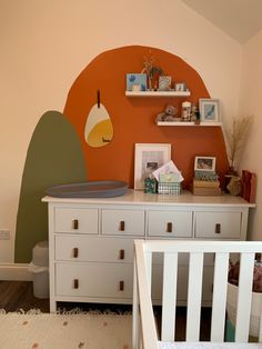 a baby's room with an orange wall and white dresser