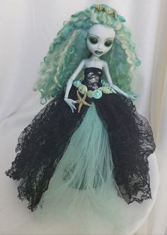 a doll with green hair wearing a black dress and starfish in her hand on a white background