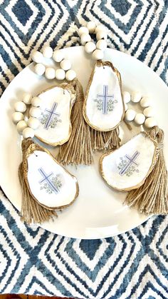 three pieces of shell with tassels and beads on a white plate next to a blue patterned tablecloth