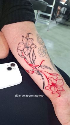 a person with a flower tattoo on their arm next to a white phone and camera