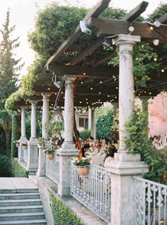 an outdoor dining area with lots of seating and lights on the ceiling, surrounded by greenery