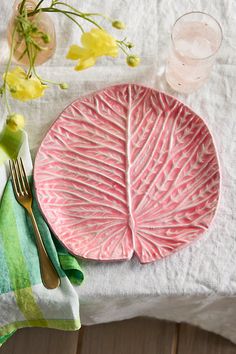 a pink plate sitting on top of a white table cloth next to a fork and knife