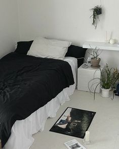 a bedroom with white walls and black bedspread, potted plants on the floor