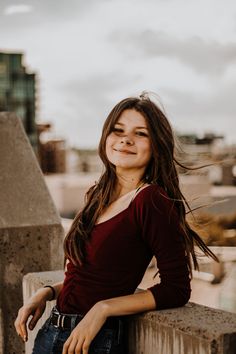 a woman leaning on a wall with her hair blowing in the wind and looking at the camera