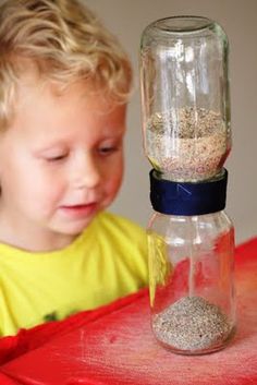 a young boy looking at a jar with sand in it and a bird feeder on top