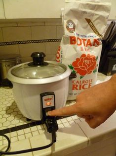 a person is pointing at an electric rice cooker on the counter next to a bag of rice