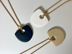 three necklaces with different shapes and colors on the same chain, one is white, one is blue