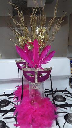 a stove top with a vase filled with pink feathers and some gold decorations on it