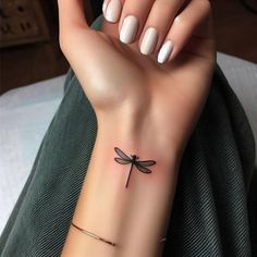 a woman's arm with a small dragonfly tattoo on her left wrist and white nails