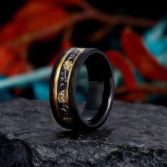 a black and gold wedding ring sitting on top of a rock