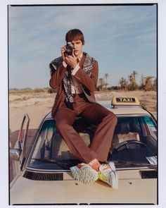 a man sitting on top of a car holding a camera