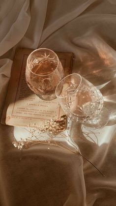 two wine glasses sitting on top of an open book next to a glass filled with water