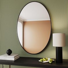 a round mirror sitting on top of a black table next to a lamp and book