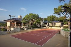 a tennis court surrounded by lots of trees and houses in the background with lights on either side