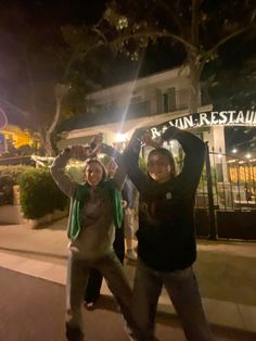 two people standing on the sidewalk with their arms in the air and smiling at the camera