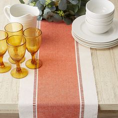 the table is set with yellow glasses and orange placemats on top of it