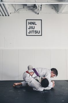 two men in white shirts and black pants are doing a side control on the ground