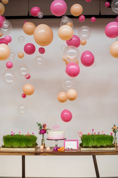 a table topped with lots of balloons and grass covered in pink, white and orange