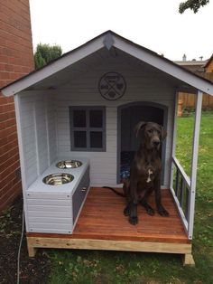 a dog house with a large black dog sitting in it's doorway and two bowls on the outside