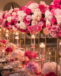 a table topped with tall vases filled with pink and white flowers next to candles