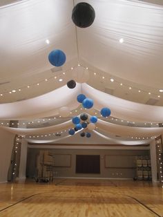 an indoor basketball court is decorated with blue and white balls, lights, and draping