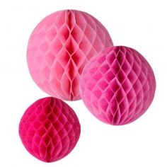 three pink honeycombs hanging from strings on a white wall in the shape of balls