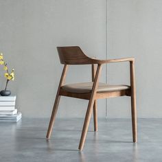 a wooden chair next to a stack of books and a vase with yellow flowers in it