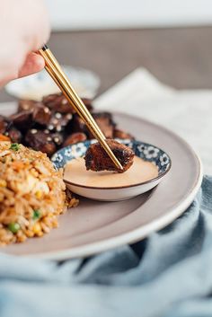 someone is holding chopsticks over a plate of food with rice and meat on it