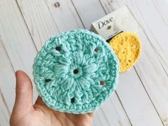 a hand holding a crocheted button in front of a white wooden background with two yellow buttons