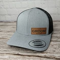 a gray and black trucker hat with brown leather patch on the front that says groom