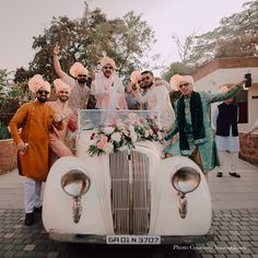 a group of people standing in front of a white car with flowers on the hood