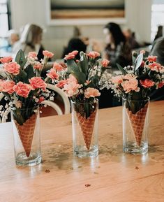 three vases filled with flowers sitting on top of a wooden table next to each other