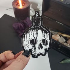 a hand holding up a sticker with a skull on it next to a candle