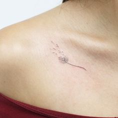 a woman with a small tattoo on her chest holding a dandelion in one hand