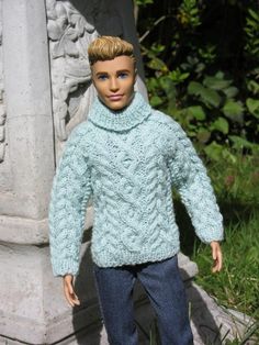 a doll wearing a sweater and jeans standing in front of a stone pillar with a statue behind it