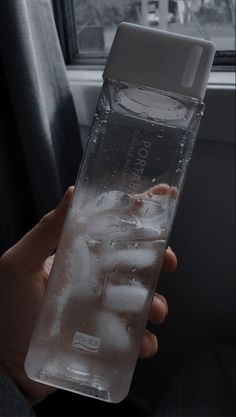 a person holding a water bottle with ice in it and the lid partially covered by plastic