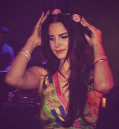 a woman with long dark hair wearing a colorful dress and holding her hands up to her head