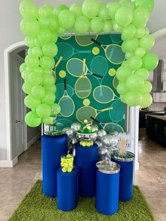 a tennis themed party with green balloons and blue cylinder vases filled with snacks on the floor