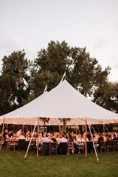 a group of people sitting at tables under a large white tent with lights on it