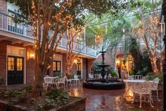 an outdoor courtyard with tables and chairs, lights strung from the ceiling and potted trees