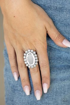 a woman's hand wearing a ring with an oval stone surrounded by small diamonds